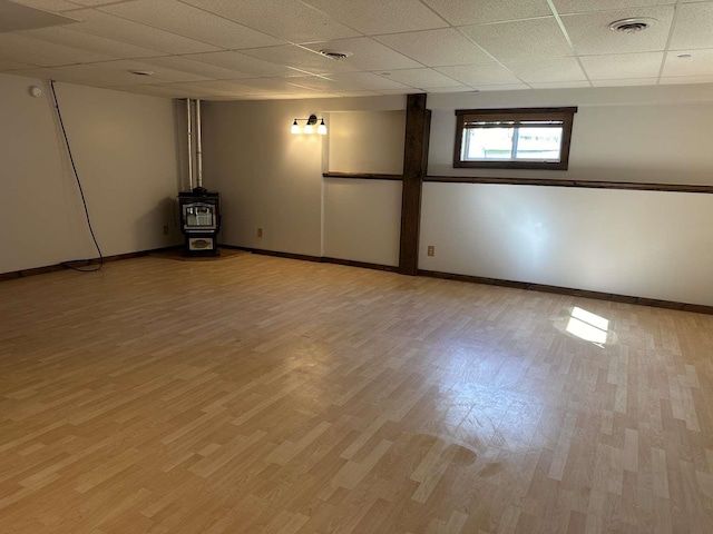 basement featuring a paneled ceiling, a wood stove, and light hardwood / wood-style flooring