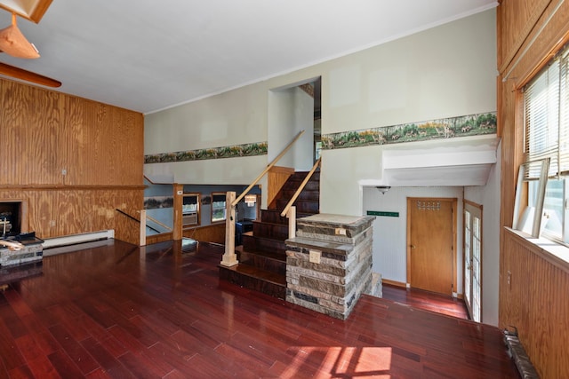 interior space with a stone fireplace, crown molding, dark wood-type flooring, a baseboard heating unit, and wooden walls