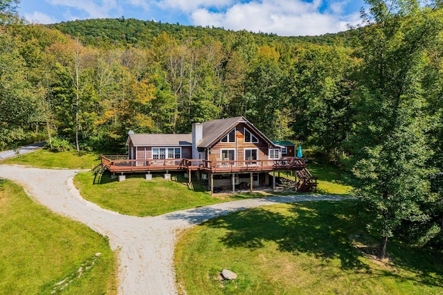 rear view of house featuring a forest view, driveway, and a deck