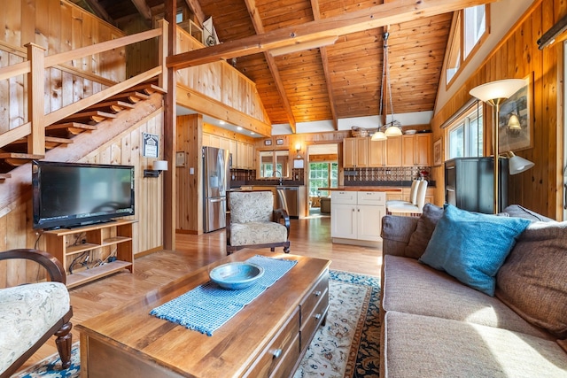 living area featuring wooden walls, wooden ceiling, light wood-type flooring, lofted ceiling with beams, and stairs