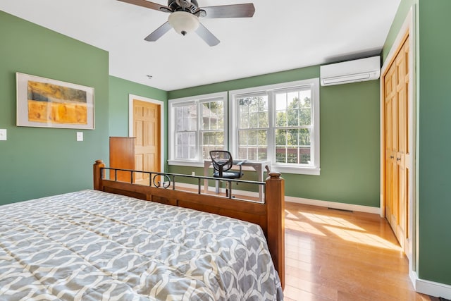 bedroom with a wall mounted air conditioner, light wood-style floors, ceiling fan, baseboards, and visible vents