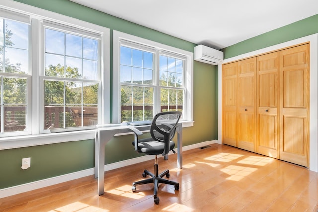 office space featuring baseboards, plenty of natural light, light wood finished floors, and a wall unit AC
