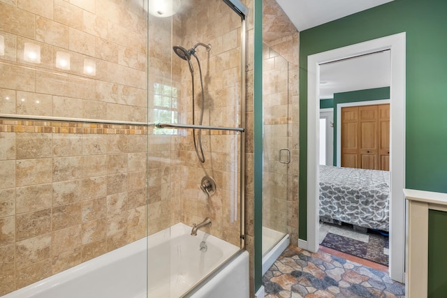 ensuite bathroom with combined bath / shower with glass door, stone finish flooring, and ensuite bathroom