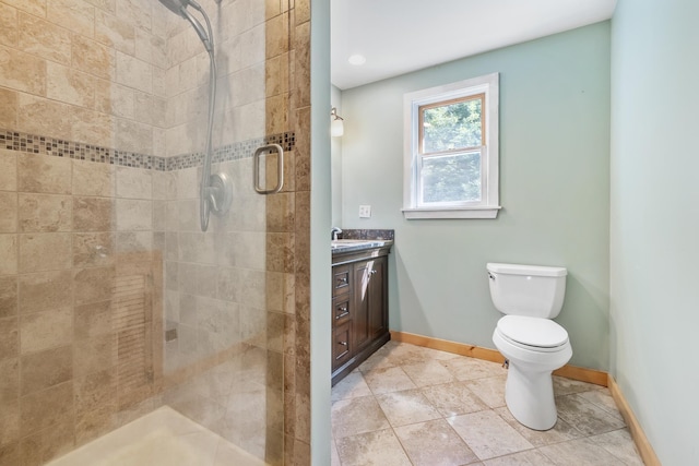 bathroom with toilet, vanity, baseboards, tile patterned flooring, and tiled shower