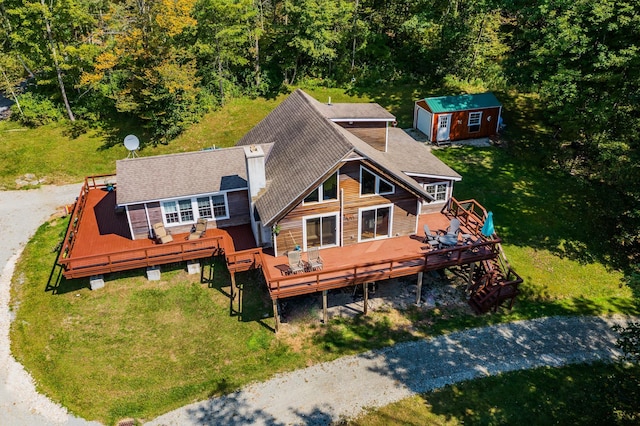 rear view of property featuring an outdoor structure, a lawn, roof with shingles, and a deck