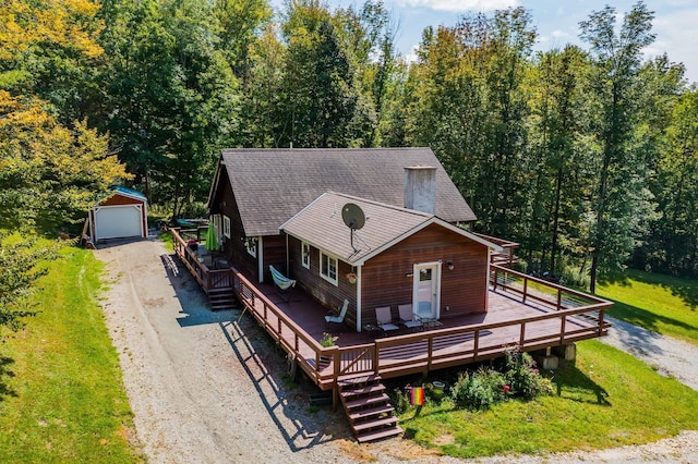 chalet / cabin with driveway, a deck, an outbuilding, a garage, and roof with shingles