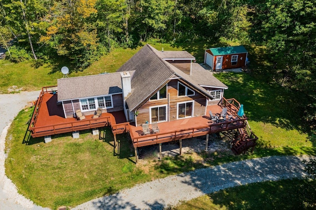 rear view of house with a wooden deck, roof with shingles, an outbuilding, and a yard