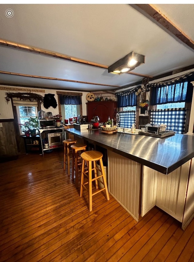 kitchen with dark wood-type flooring, wood walls, and a breakfast bar