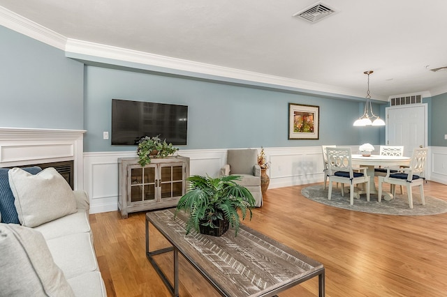 living room with light wood-type flooring, crown molding, and an inviting chandelier