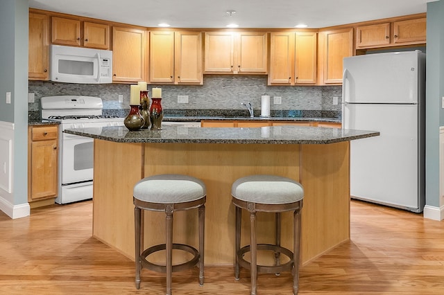 kitchen with light wood-type flooring, white appliances, a center island, and a breakfast bar area