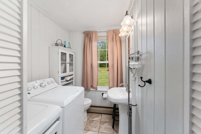 washroom featuring baseboard heating, light tile patterned floors, crown molding, wooden walls, and washer and dryer