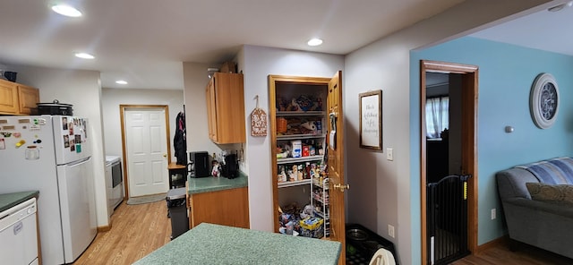 kitchen with washer / dryer, white appliances, and light hardwood / wood-style flooring