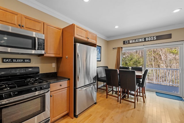 kitchen with ornamental molding, light wood-type flooring, dark stone countertops, and appliances with stainless steel finishes