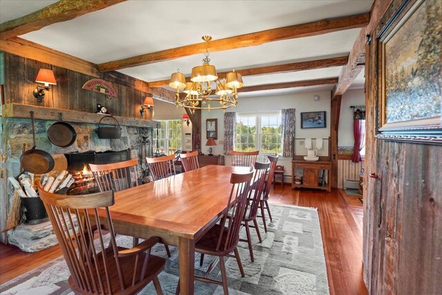 dining room with beamed ceiling, wood walls, a notable chandelier, a fireplace, and hardwood / wood-style floors