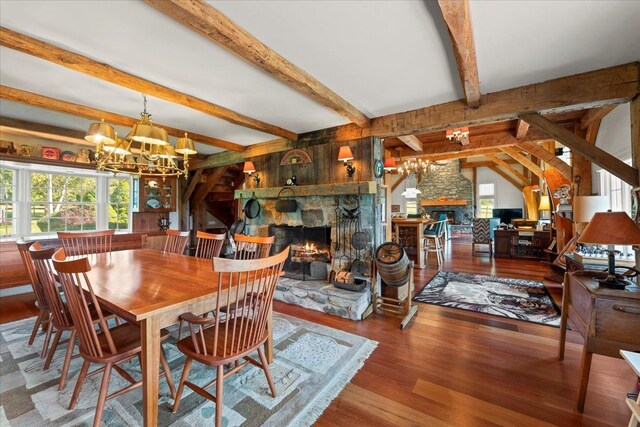 dining room with wood-type flooring, a stone fireplace, lofted ceiling with beams, and a chandelier