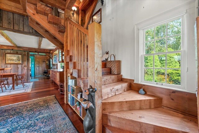 stairway with wooden walls, beamed ceiling, and hardwood / wood-style flooring