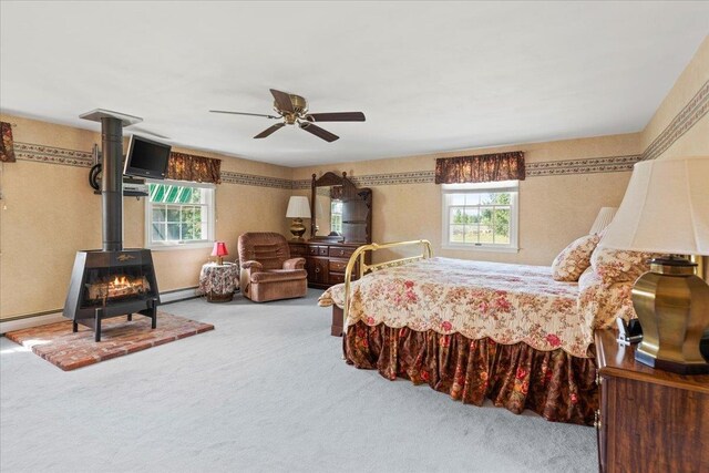 carpeted bedroom featuring ceiling fan, a wood stove, and multiple windows