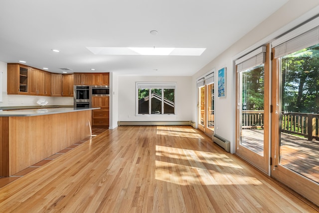 kitchen featuring light hardwood / wood-style floors, a skylight, tasteful backsplash, baseboard heating, and stainless steel double oven