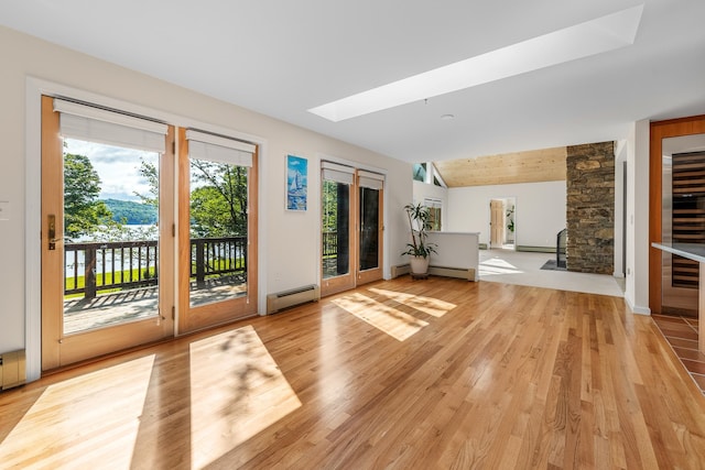 unfurnished living room with baseboard heating, light wood-type flooring, and lofted ceiling with skylight