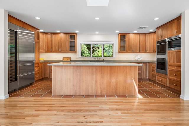 kitchen with decorative backsplash, a center island, stainless steel appliances, sink, and light hardwood / wood-style flooring