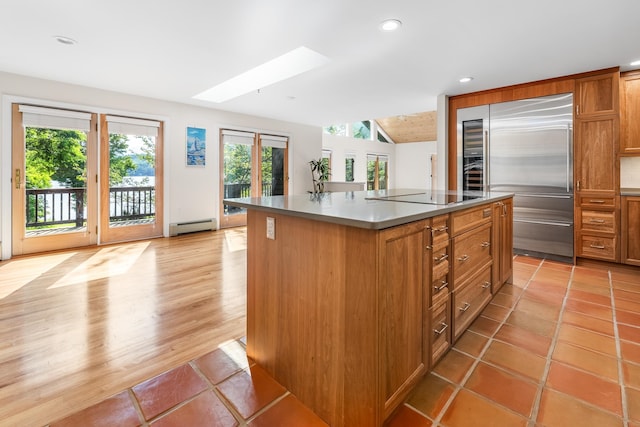 kitchen featuring stainless steel built in refrigerator, light hardwood / wood-style flooring, a center island, a baseboard heating unit, and black electric stovetop