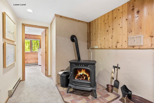 details with wood walls, baseboard heating, carpet flooring, and a wood stove