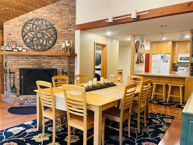 dining space featuring a brick fireplace, light hardwood / wood-style floors, lofted ceiling, stacked washer and clothes dryer, and brick wall