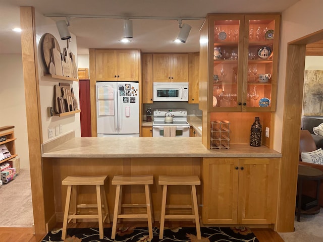 kitchen with wood-type flooring, white appliances, a breakfast bar, rail lighting, and kitchen peninsula