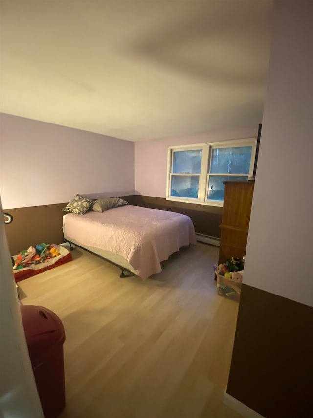 bedroom featuring a baseboard heating unit and hardwood / wood-style flooring