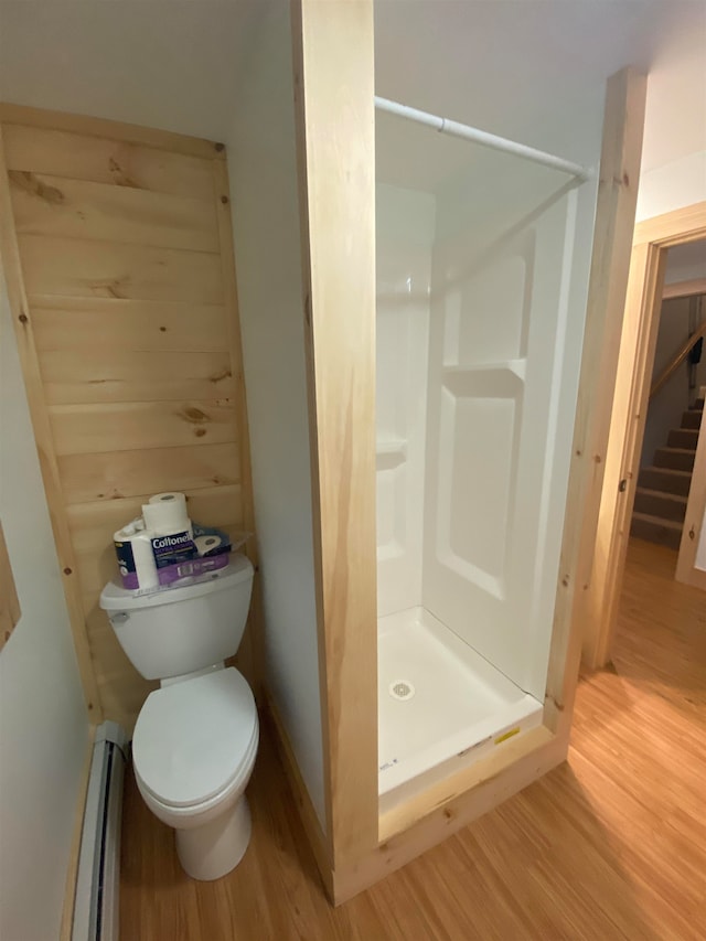 bathroom with a baseboard heating unit, wood-type flooring, a shower, and toilet