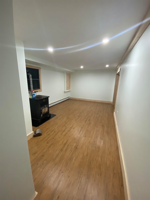 basement featuring a baseboard heating unit, hardwood / wood-style flooring, and a wood stove