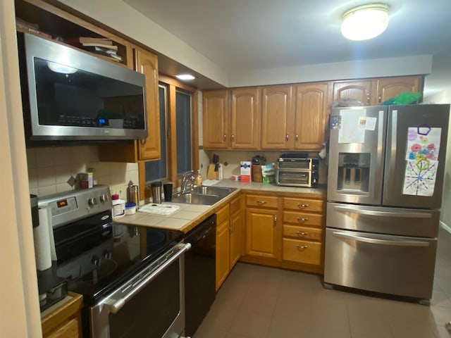 kitchen featuring tile counters, light tile patterned flooring, sink, backsplash, and appliances with stainless steel finishes