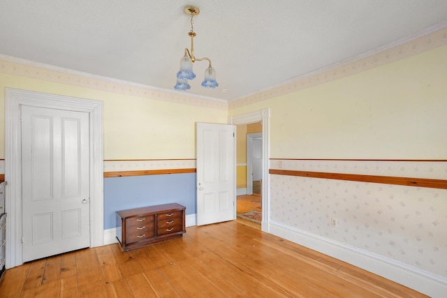 empty room with a notable chandelier, light wood-type flooring, crown molding, and a textured ceiling