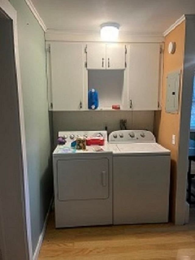 laundry room featuring electric panel, ornamental molding, cabinets, washing machine and dryer, and light wood-type flooring