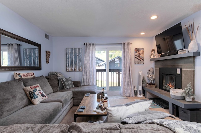 living room with recessed lighting, visible vents, a textured ceiling, and a glass covered fireplace