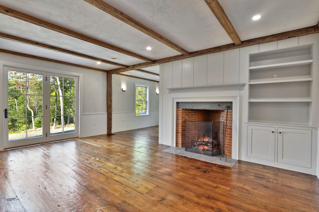 unfurnished living room with hardwood / wood-style flooring, beam ceiling, built in shelves, and a brick fireplace