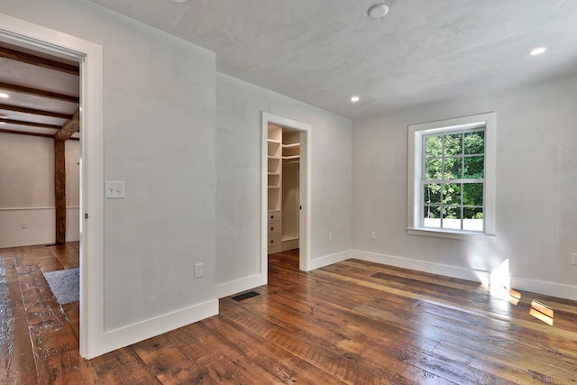 unfurnished bedroom with a walk in closet, dark wood-type flooring, and beam ceiling