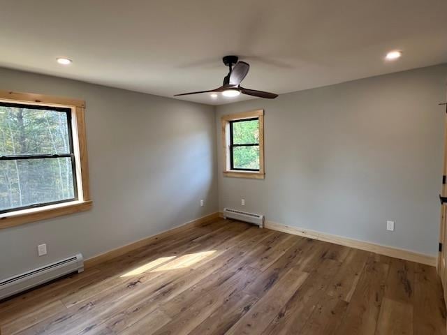 empty room with ceiling fan, light wood-type flooring, and a baseboard heating unit