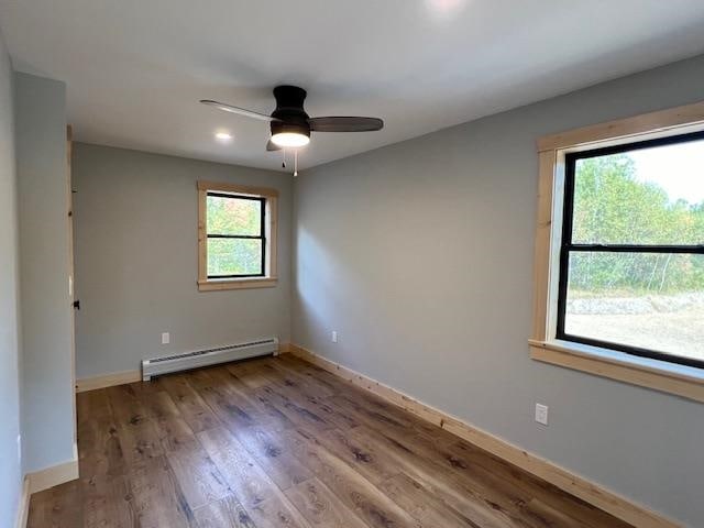 empty room featuring wood-type flooring, ceiling fan, and a baseboard heating unit