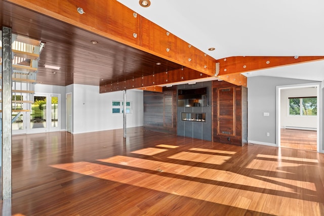 unfurnished living room with wood-type flooring, plenty of natural light, vaulted ceiling, and a baseboard heating unit