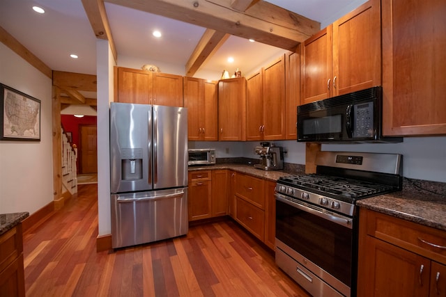 kitchen featuring dark stone countertops, hardwood / wood-style floors, beamed ceiling, and stainless steel appliances