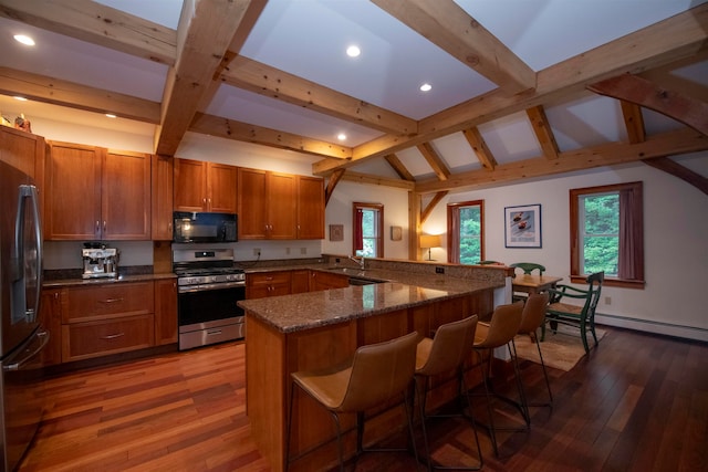 kitchen with kitchen peninsula, appliances with stainless steel finishes, a kitchen breakfast bar, dark stone countertops, and hardwood / wood-style floors