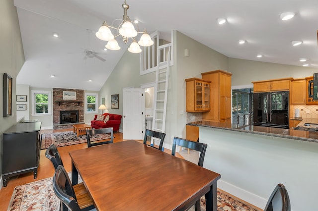 dining area featuring ceiling fan with notable chandelier, light wood-type flooring, high vaulted ceiling, and a fireplace