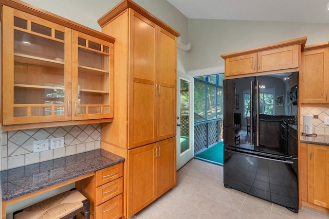 kitchen featuring light tile patterned flooring, lofted ceiling, backsplash, dark stone countertops, and black refrigerator