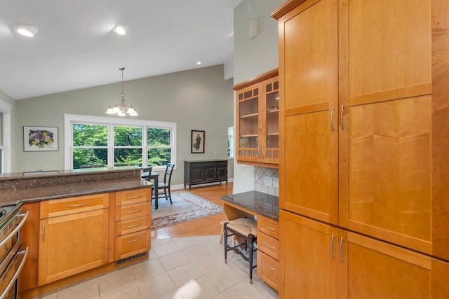 kitchen featuring pendant lighting, stainless steel stove, lofted ceiling, dark stone counters, and a notable chandelier