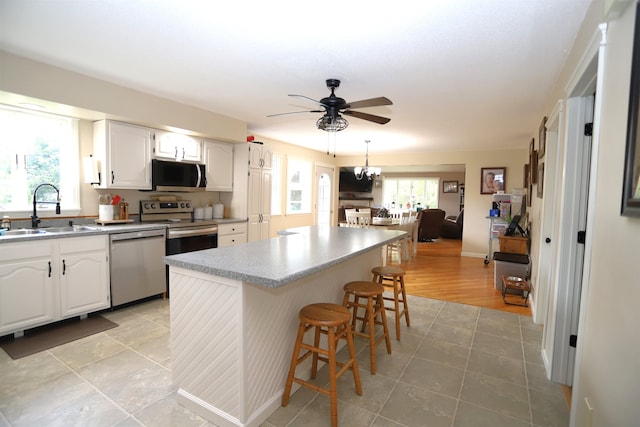 kitchen featuring appliances with stainless steel finishes, white cabinetry, ceiling fan with notable chandelier, a kitchen bar, and sink