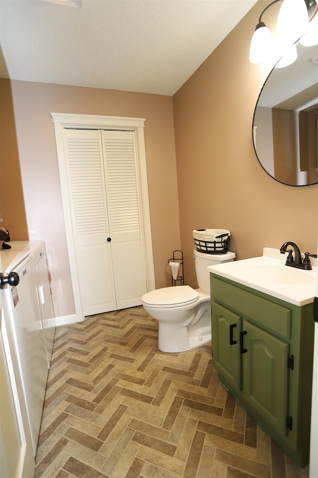 bathroom with a textured ceiling, parquet flooring, independent washer and dryer, vanity, and toilet