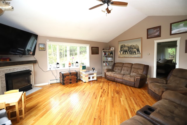 living room with light hardwood / wood-style floors, vaulted ceiling, a baseboard radiator, a stone fireplace, and ceiling fan