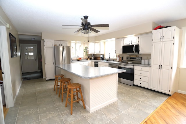 kitchen featuring white cabinetry, a kitchen island, a kitchen breakfast bar, stainless steel appliances, and ceiling fan