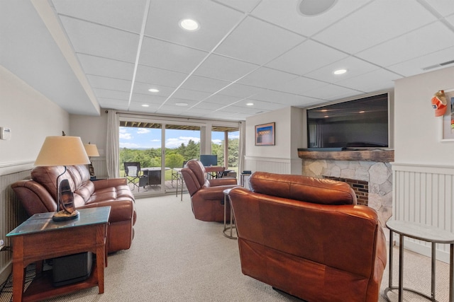 living room with a paneled ceiling, carpet flooring, and a stone fireplace